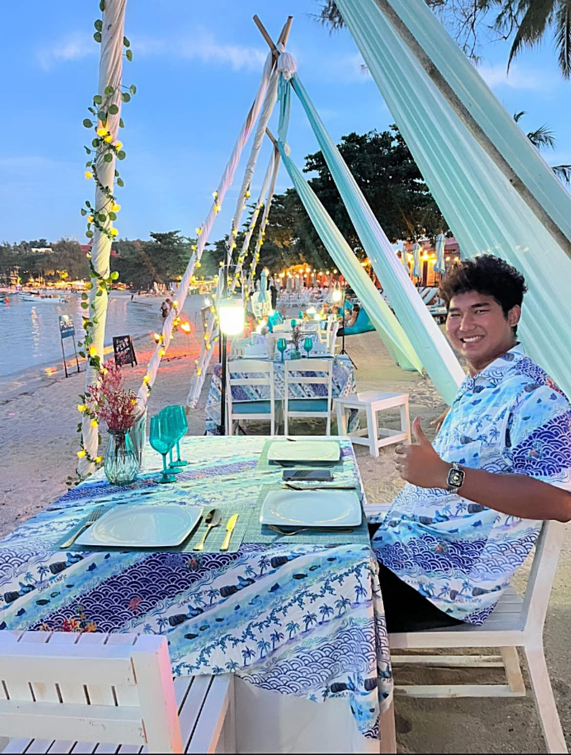 Tables set under the tent canopy at dusk — fairy lights on, beach ready