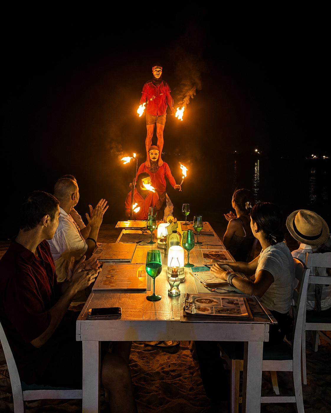 Artistas de fuego justo delante de una mesa ocupada frente al mar por la noche