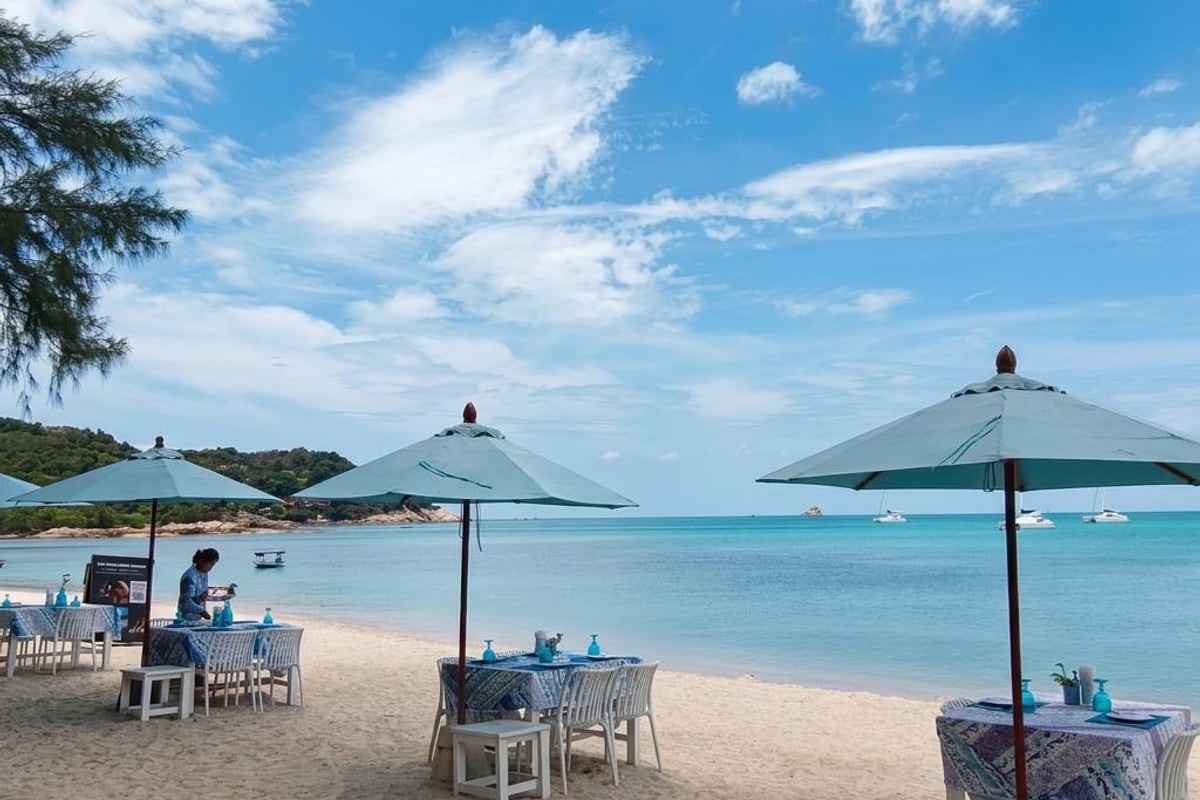 Mesas de almuerzo en la arena bajo sombrillas en The Blue Spice Samui, playa de Choeng Mon