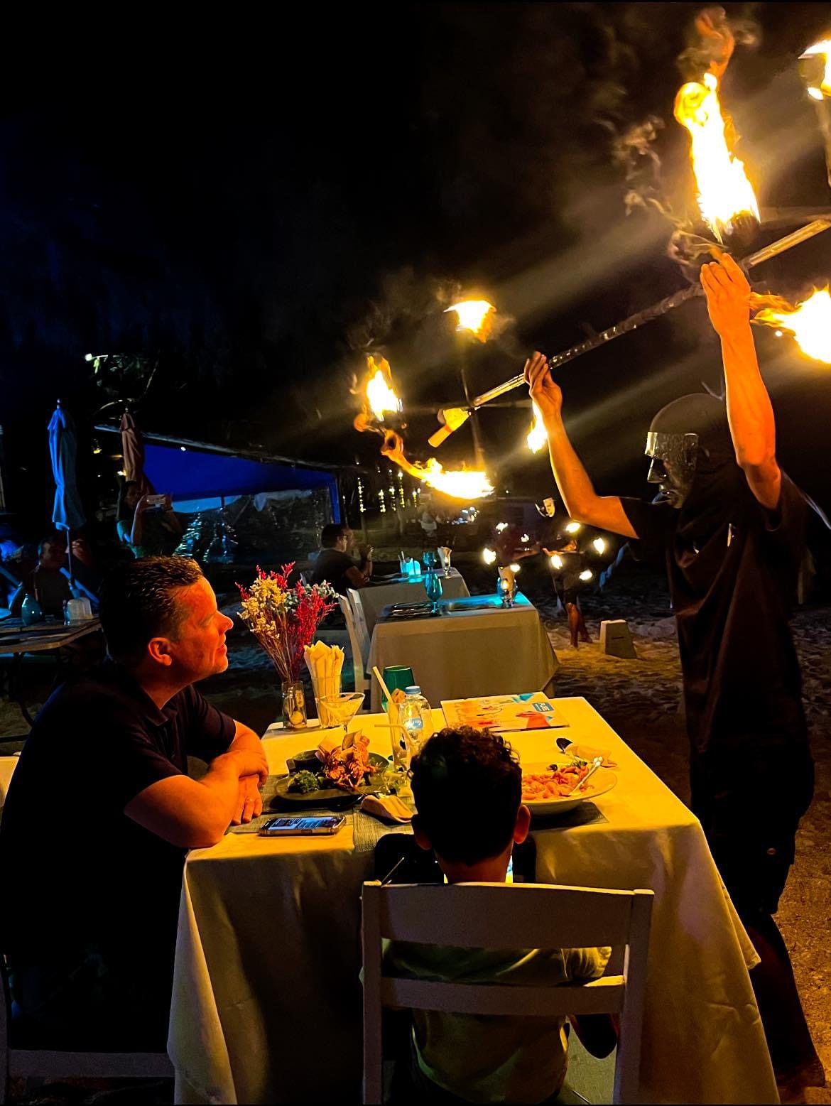 Fire show performer at a dining table — guests watching at The Blue Spice, Choeng Mon Beach
